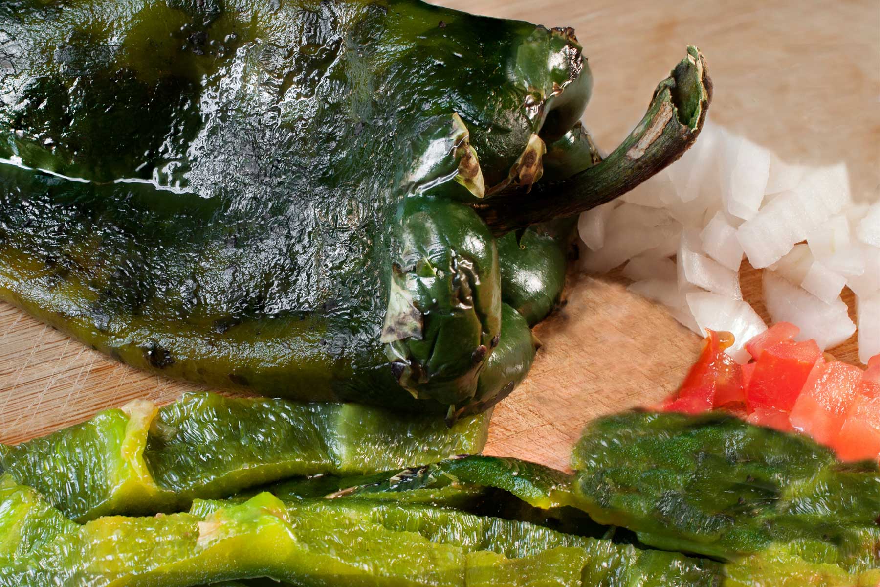 Roasted and peeled poblano chile and slices of oven roasted poblano pepper on a cutting board 